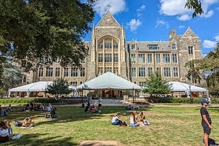 College campus with students on a grass lawn in front of a majestic stone building