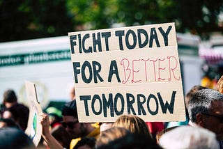 a cardboard protest sign in a crowd that says “Fight today for a better tomorrow”