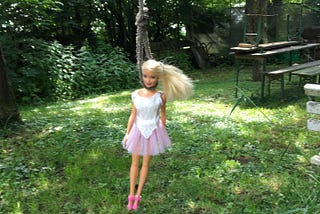 A barbie doll hanging on a tree by its neck.