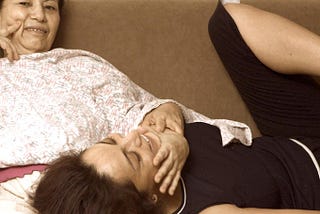 Mother left, and daughter lies on her lap. Daughter is about thirty years old.