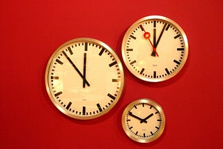 Three analog clocks of various sizes positioned against a red background.