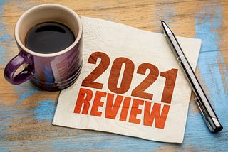 review of 2021 written on a napkin, alongside a cup of black coffee and a pen