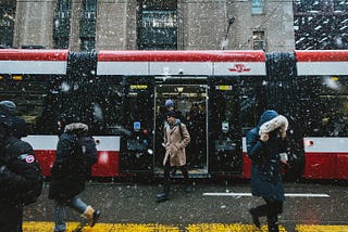 People walking in the snow outside of a streetcar in downtown Toronto