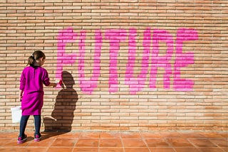 Young girl painting the word “Future” on a brick wall