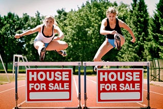 Two women jumping over a hurdle with “House For Sale” sign attached
