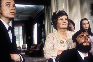 A still from the film “My Left Foot.” A man in a suit stands on the left side while a woman leans on the wheelchair of the main character, Christy Brown, played by Daniel Day-Lewis.