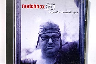 Album Cover for MatchBox 20 featuring a man in a fitting leather cap with glasses with his eyes closed. The cover is an indigo color.