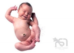 Newborn baby boy floating on white background, peeing into the air