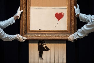 Photo of Banksy’s painting “Girl with Balloon” after it’s been shredded. It’s carried by 2 Sotheby’s employees, taking care of the newly created piece of art called “Love Is in the Bin”, carrying the art-piece with white gloves and showcasing it.