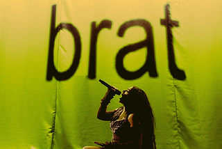 Album cover of Charli XCX’s Brat, featuring Charli in a fierce pose with a green background and the word brat which is the album cover