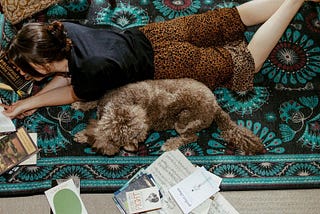 Linea laying on the floor reading surrounded by books and her dog