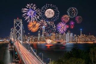 Ten fireworks exploding above a city skyline at night, with a bridge in the foreground