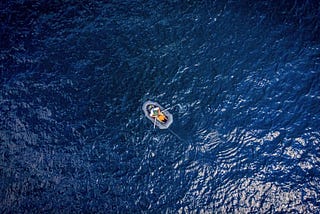 Featured image: An aerial photograph of a rubber dinghy alone on the deep blue open ocean.