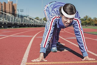 A person in a track suit preparing to run on a track.