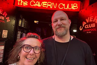Me standing outside the legendary Cavern Club in Liverpool, smiling under the glow of the red neon sign. Next to me is a serious-faced bouncer in black, guarding the entrance to one of the most iconic music venues in the world. Beatles energy in the bricks.