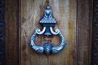 A closed wooden door with a brass knocker, representing institutional access and support that exist but not necessarily available