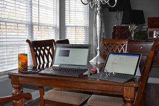 A dining room with two laptops opened on the table and a pair of glasses on one of the computers