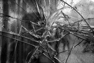 A black and white image of shattered glass or ice. The splintered lines serve as a metaphor for the way we are fractured as we move through life collecting trauma wounds.