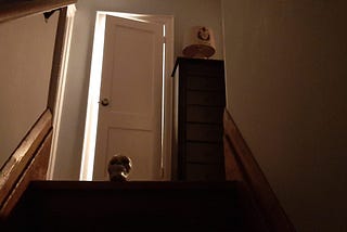 A shot up a short flight of stairs with a skull at the top and a half-closed, backlit, door behind it.