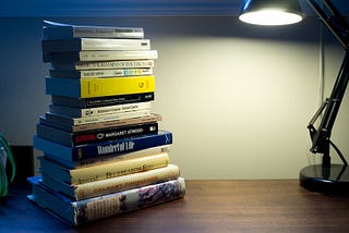 A stack of books on a desk, lit by a desk lamp
