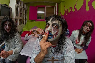 Man smoking in a zombie costume surrounded by two zombie women.