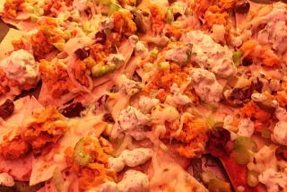 A pan of nachos with melted cheese, olives, celery, and dots of white ranch dressing.