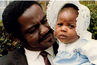 Black man holding Black baby who is looking at the camera