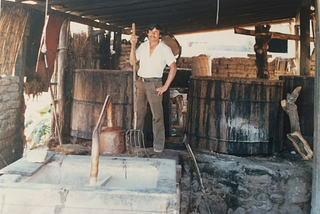 Manuel Santiago Hernandez, my father, in his palenque circa 1984. He’s standing between two wooden vats–used to ferment the mashed agave–holding a pitchfork, February, 1984.