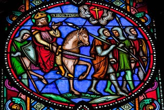 Photo of a stained-glass window that depicts a warrior wearing a crown and riding a horse along with four armored soldiers carrying spears and shields.