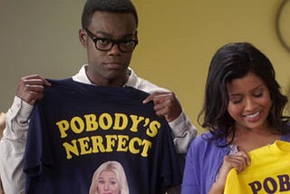 Still from the TV show “The Good Place.” Characters Chidi and Tahani hold up t-shirts that say “Pobody’s Nerfect.”