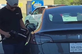 A man trying to fuel a Tesla with a gasonline pump.