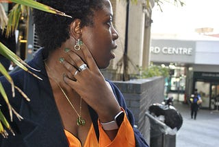 Scribe posing showing their natural hair, wearing an orange shirt and navy wool long coat