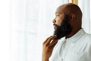 jclay in white holding beard looking out the window