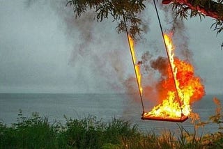 imagem de um balanço pegando fogo numa paisagem aberta ao fundo há o mar