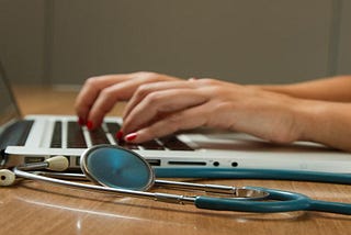 hands typing on laptop keyboard with stethoscope nearby