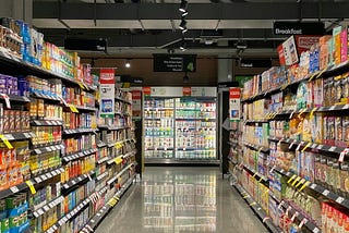 A photo of a supermarket isle with products on both sides and a dairy cooler at the end