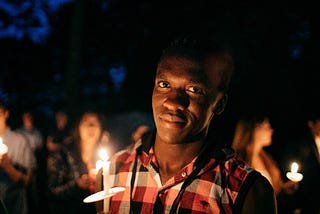 African man holding a candle at a night vigil.