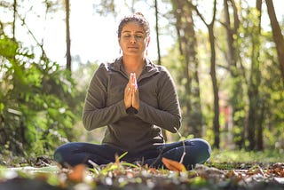 Woman sitting cross legged, hands joined, eyes closed in sitting meditation