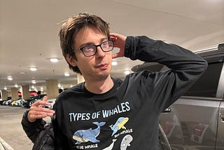 man with glasses wearing a whales shirt in parking lot
