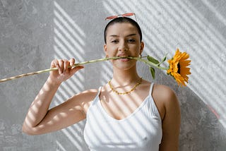 A fierce woman with a sunflower; she is biting the stem with her teeth.