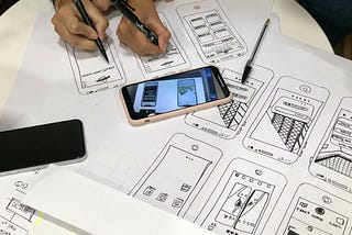 People sketch phone interfaces on a table together