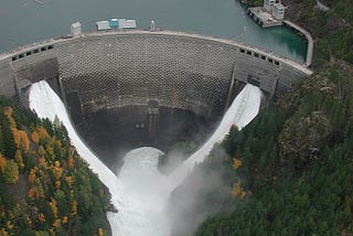 A large hydroelectric reservoir dam, with water exiting thru its partly opened spillways.