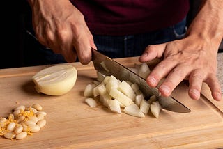 Man chopping onions with a chef’s knife on a wood cutting board.