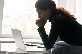Financial problem. Thoughtful hispanic woman sit by home laptop lean on clasped hands consider on tax loan credit debt. Upset young lady freelancer understand her small business is close to bankruptcy