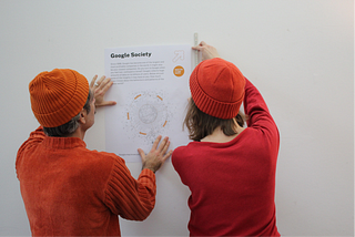 Two colleagues hanging up one of the What the Future Wants posters; photo courtesy of Daisy Kidd