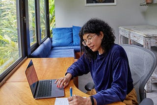 A woman checks off a list while looking at a laptop screen
