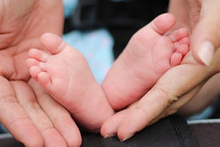 A newborn’s feet are cradled by a parent’s hands.