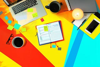 Top view of a laptop, notebook, coffee cups, and post-it notes on a desk
