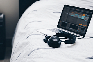 Ableton Live on a laptop sitting on a bed with headphones next to it.