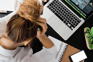 Person sits in front of computer with their head down, looking stressed.